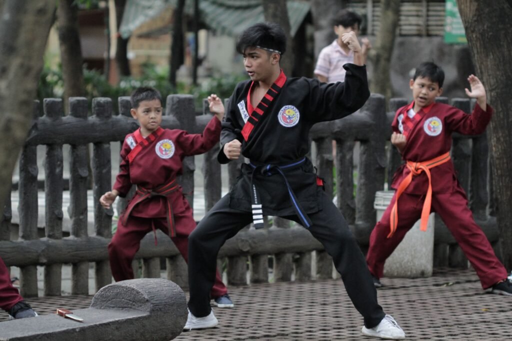 Dua pesilat memperagakan teknik serangan dan pertahanan di kawasan pesisir dengan mengenakan busana bernuansa tradisional.